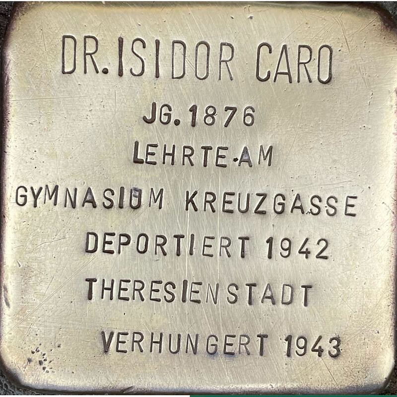 Isidor Caro (6.10.1876 in Żnin gestorben am 28.08.1943 in Theresienstadt) war ein deutscher Rabbiner der jüdischen Gemeinde Köln und Religionslehrer am Gymnasium Kreuzgasse. Er war mit Klara Beerman verheirate, das Ehepaar hatte zwei Kinder, Hermann und Rut, und wohnte auf Ehrenfeldgürtel 171. Isidor und Klara Caro widmeten sich bis 1938 intensiv der seelsorgerischen Tätigkeit. Während des Novemberpogroms 1938 fiel Dr. Caro durch seine besonnene, furchtlose Art auf, er wollte seine inhaftierten Glaubensbrüder besuchen und ließ sich auch durch Drohungen nicht einschüchtern. Schon vor 1941 mussten ihre Wohnung verlassen und wohnten dann im Hinterhaus der Synagoge Roonstraße 50, mit 13 anderen Personen auf sehr kleinem Raum. Im Juni 1942 wurde der erste Transport jüdischer Kölner nach Theresienstadt aufgerufen. Die Caros hatten sich freiwillig zur Begleitung des ersten »Judentransports« zur Verfügung gestellt. Isidor Caro verstarb am 28. August 1943, er ist verhungert, seine Frau Klara überlebte und zog nach 1945 zu ihrer in die USA geflohenen Tochter. Der Sohn Hermann, Schüler der Kreuzgasse, wurde im Konzentrationslager Auschwitz ermordet. Quelle: Der gesamte Text fusst auf dem Eintrag „Isidor Caro“ auf Wikipedia.com und Kirsten Serup-Bilfeldt: Stolpersteine, Köln 2003, S. 33 – 40, Informationen des NS-Dokumentationszentrums Köln, den Einträgen in Yad-Vashem & Arolsen-Archives.