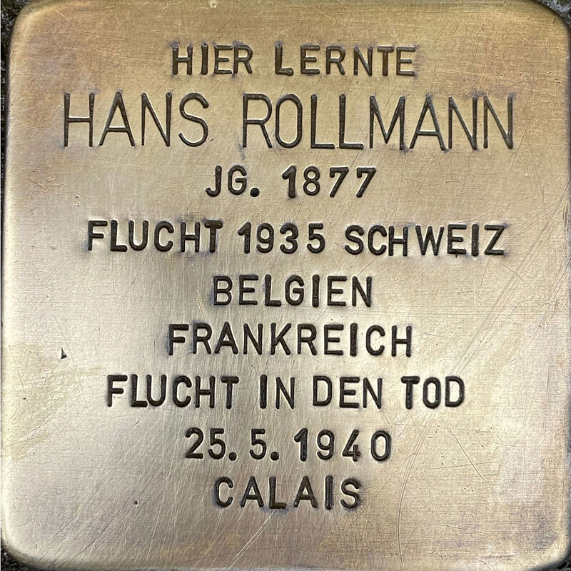 Hans Rollmann (geboren am 10.8.1877 in Köln, gestorben am 3.09.1944 in Calais) wurde nach dem Schulabschluss an der Kreuzgasse wie sein Vater Schuhfabrikant und war Miteigentümer der bekannten Schuhfabrik ROMIKA. Er heiratete Marie Hertz und ihre drei Söhne Ernst, Heinz und Klaus besuchten auch die Kreuzgasse. Hans Rollmann stand der SPD nahe und Jude, deswegen und weil die Nationalsozialisten schnell auf seine lukrative Fabrik aufmerksam wurden, wurde ab 1933 seine Fabrik schnell in Zahlungsschwierigkeiten gebracht, er selbst verleumdet, als Verbrecher diffamiert und per Haftbefehl gesucht. Hans Rollmann griffen diese Schwierigkeiten auch gesundheitlich an. Er floh in die Schweiz und musste von dort aus zu sehen, wie ihm sein Besitz widerrechtlich entzogen wurde. Die Rollmanns zogen nach Belgien und eröffneten dort eine Schuhfabrik. Nach dem deutschen Überfall auf Belgien flohen die Söhne in die USA, der schwer erkrankte Hans Rollmann und seine Ehefrau beginnen gemeinsam Suizid.  Quelle: Der gesamte Text fußt auf Informationen der Dokumentation dieser Enteignung: Heinz Ganz-Ohlig: ROMIKA – „eine jüdische Fabrik“, Trier 2012, Informationen im Gedenkbuch der Kreuzgasse und Informationen des NS-Dokumentationszentrums Köln.
